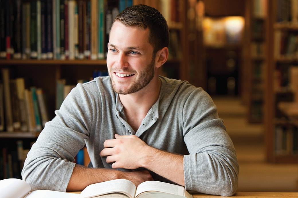 A man at the library smiling with books on the table
